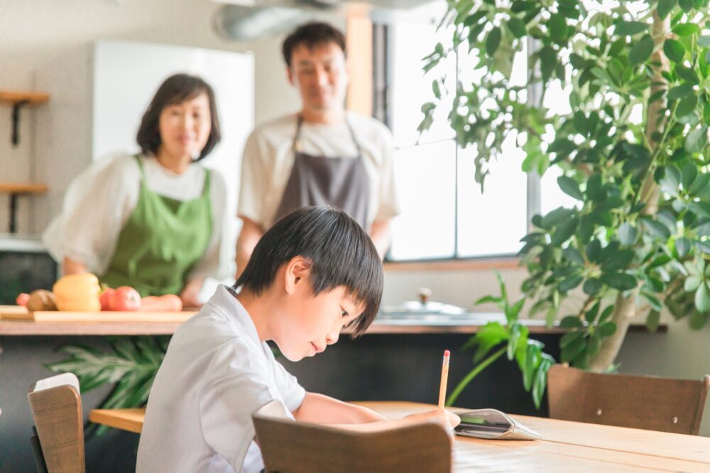 自宅で両親に見守られながら勉強している小学生